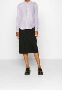 Gestreepte blouse met lange mouwen in rood, blauw en wit; zwarte kokerrok; zwarte loafers. Gladde stof en perfecte pasvorm.