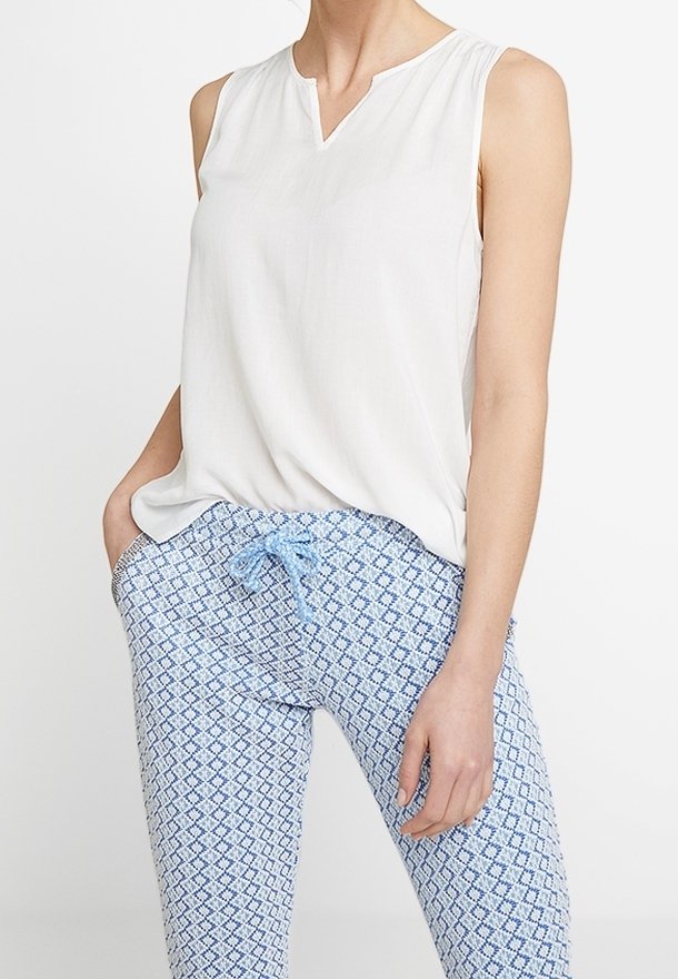 Blouse blanche sans manches avec col en V, associée à un pantalon bleu clair à motifs avec un design en losange et une taille à cordon.