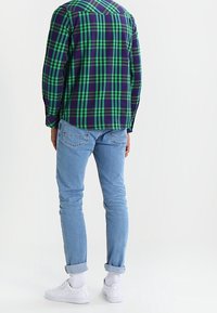 Zielona i granatowa koszula w kratę z kołnierzykiem zapinanym na guziki, zestawiona z jasnoniebieskimi dżinsami i białymi trampkami. Ubranie charakteryzuje się podwiniętymi rękawami.