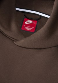 Sweatshirt Nike marron avec un col montant, étiquette avec logo, taille M et instructions d'entretien. La texture du tissu est lisse et légère.