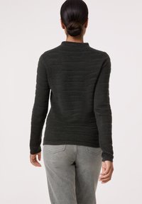 Dunkelgrüner, texturierter Pullover mit einem gerippten Muster, langen Ärmeln und einem runden Halsausschnitt, kombiniert mit hellgrauen Jeans.