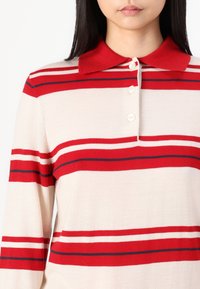 Long-sleeve polo shirt in cream with red and navy horizontal stripes, featuring a red collar and three front buttons. Soft knit texture.