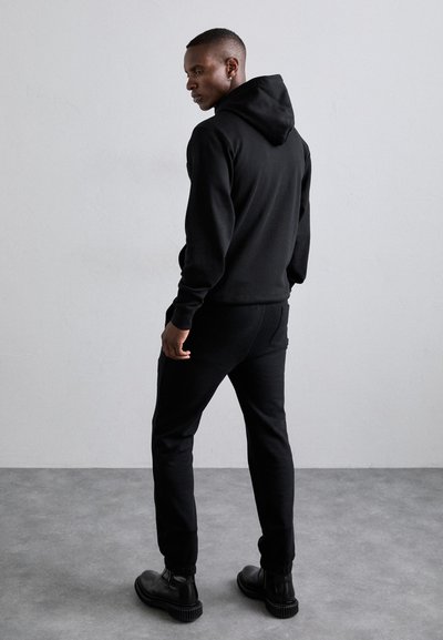 Hanorac negru cu glugă, cu o croială lejeră, asortat cu pantaloni sport negri. Textură netedă, design minimalist și detalii subtile de cusătură.