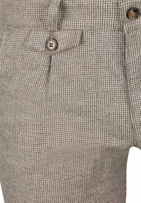 Bruine en beige geruite broek met een gestructureerde stof, voorzakken en twee knopen. Het patroon bestaat uit kleine ruiten.