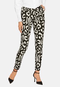 Schwarz-weiße Leopardenmuster-Hosen mit schlanker Passform, ausgestattet mit einem Knopfverschluss und Seitentaschen, kombiniert mit schwarzen High Heels.