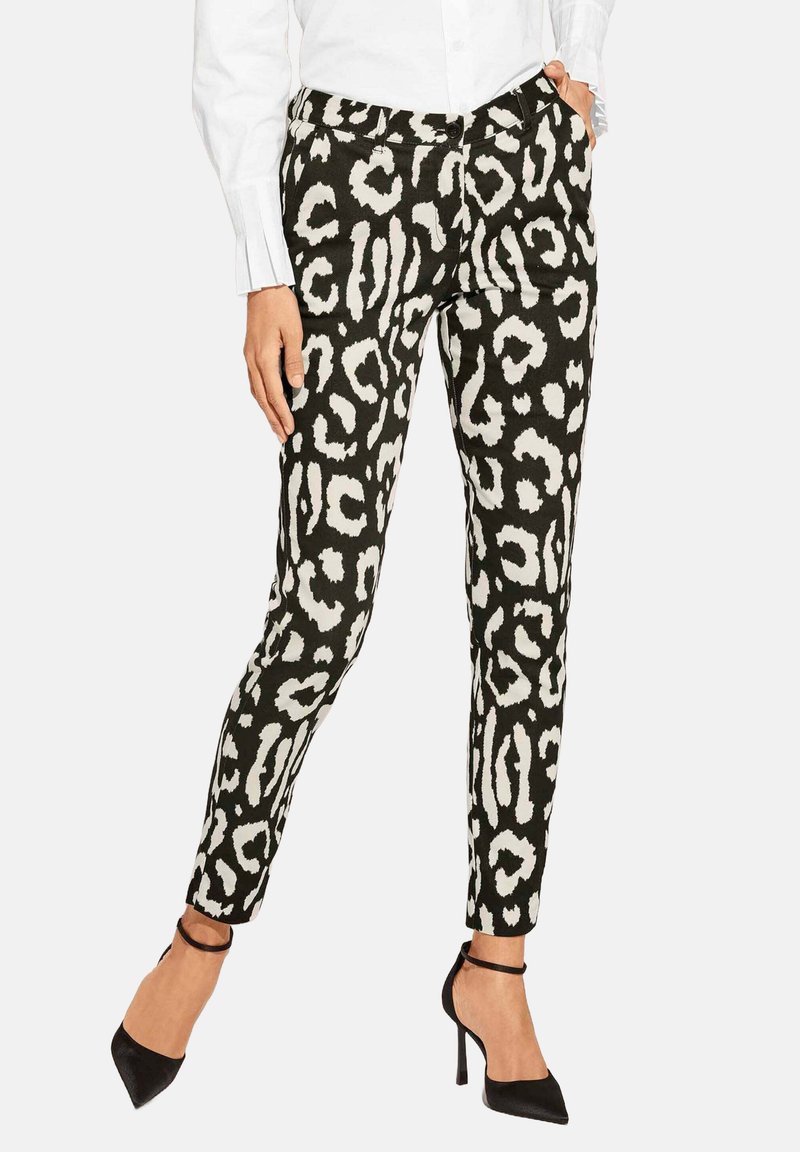 Schwarz-weiße Leopardenmuster-Hosen mit schlanker Passform, ausgestattet mit einem Knopfverschluss und Seitentaschen, kombiniert mit schwarzen High Heels.