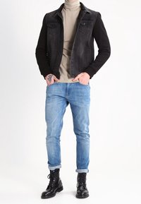 Schwarze Denimjacke mit zwei Brusttaschen, cremigem Rollkragenpullover, hellblauen Jeans und schwarzen Kampfstiefeln, mit hochgekrempelten Ärmeln.