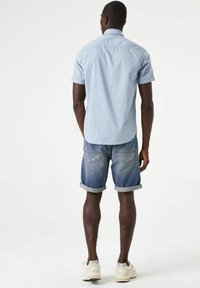Hemelsblauw shirt met korte mouwen en een geometrisch patroon, gecombineerd met denimshorts en witte sneakers. Casual outfit voor buiten.