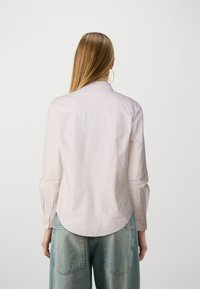 Chemise rose clair à manches longues avec un col et des détails de boutons aux poignets, assortie à un jean large bleu clair.