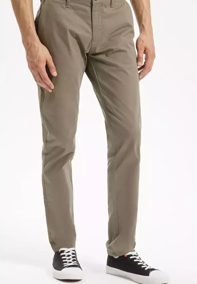 Khaki bawełniane chinosy o wąskim kroju, z przednimi kieszeniami, szlufkami na pasek oraz kontrastowymi trampkami w kolorach czarnym i białym.