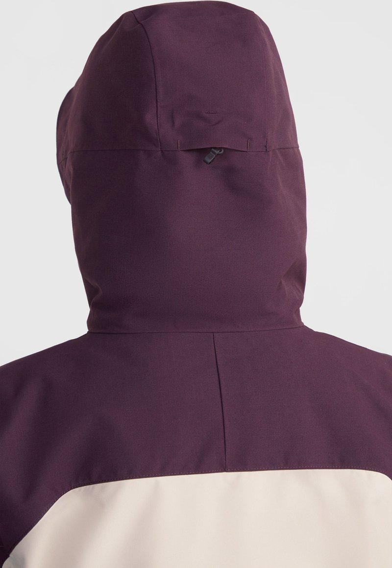 Lila wasserdichte Jacke mit strukturierter Oberfläche, ausgestattet mit einer enganliegenden Kapuze und einem kontrastierenden cremefarbenen unteren Rückenpaneel. Minimale Hardware sichtbar.