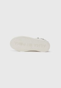 Semelle de sneaker blanche avec une texture antidérapante et un texte en relief "ALMA EN PENA" visible sur un fond blanc uni.