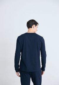 Marineblå langermet skjorte laget av mykt stoff, med rund halslinning og slank passform. Bakfra har den et minimalistisk design uten trykk.