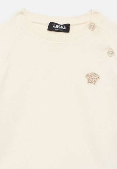 Πλεκτό πουλόβερ σε κρεμ απόχρωση με ριμπ λαιμόκοψη και μανσέτες. Διαθέτει μικρό κεντημένο χρυσό λογότυπο Medusa και λεπτομέρειες με κουμπιά στον ώμο.