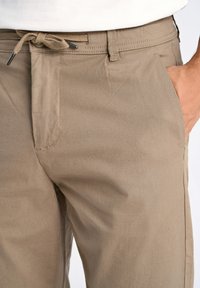 Beige lichtgewicht broek met een textuurafwerking. Beschikt over een trekkoord in de taille en zijzakken. Eenvoudig ontwerp, geen zichtbare patronen of hardware.