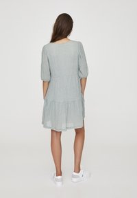 Vestido azul claro con una tela texturizada, mangas cortas abullonadas, un dobladillo en niveles y una cintura ajustada. Combinado con zapatillas blancas.