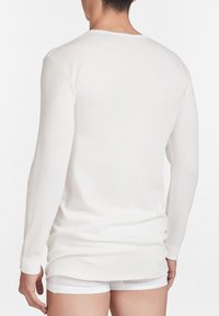 Camicia bianca in cotone a maniche lunghe con scollo rotondo, texture morbida e polsini. Il retro è semplice con un taglio leggermente allungato.