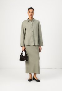 Linen button-up shirt in light olive, paired with a matching skirt. Black textured handbag with a short handle, and black flats.