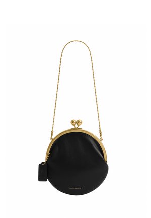 Sac à main rond en cuir noir avec cadre métallique doré et fermoir, bandoulière en chaîne dorée et petite étiquette noire attachée.