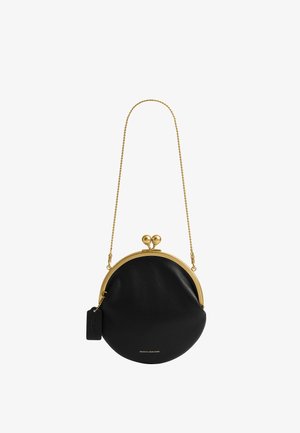 Sac à main rond en cuir noir avec cadre métallique doré et fermoir, bandoulière en chaîne dorée et petite étiquette noire attachée.