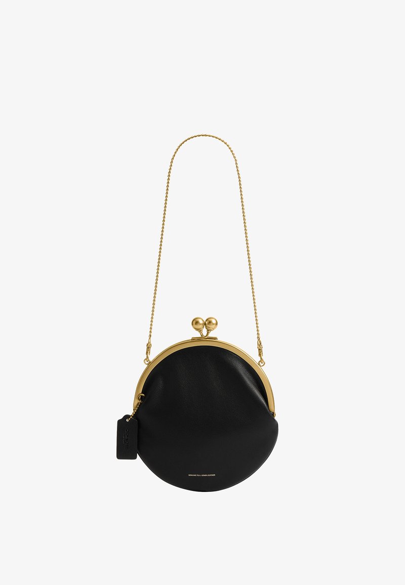 Sac à main rond en cuir noir avec cadre métallique doré et fermoir, bandoulière en chaîne dorée et petite étiquette noire attachée.