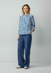 Blau-weiß gemusterte Bluse mit V-Ausschnitt und drei Viertelärmel, kombiniert mit lockeren blauen Leinenhosen und hellen Slippern.