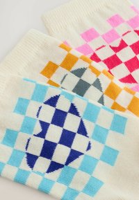 Čarape do koljena u krem boji s obojenim kariranim uzorcima. Sadrže ružičaste, narančaste, sive i plave dizajne, s kontrastnim geometrijskim oblicima.