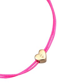 Bracelet en cordon rose avec un charme en forme de cœur doré. Le charme présente des détails gravés et une finition polie. Deux cordons s'entrelacent.
