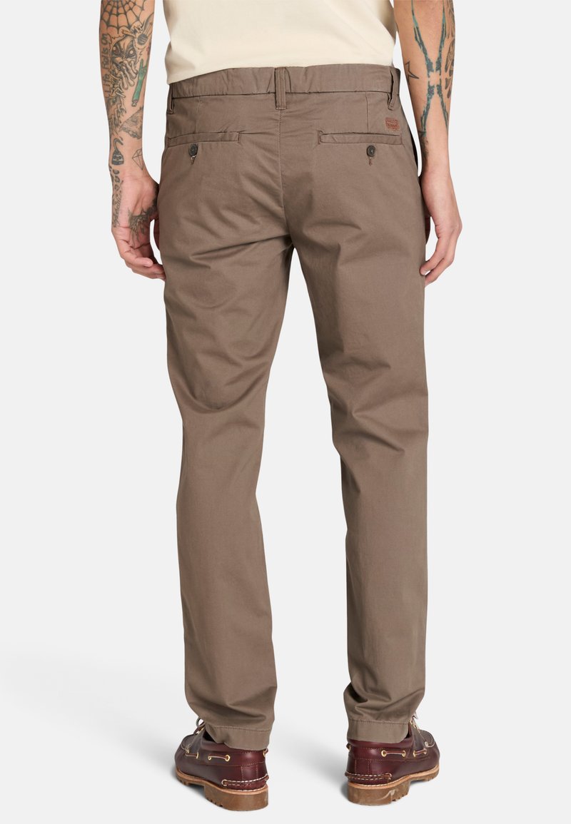 Braune Baumwollhosen im geraden Schnitt mit zwei Gesäßtaschen, getragen mit braunen Schuhen. Der Stoff ist glatt und hat eine minimale Struktur.