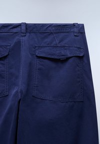 Σκούρα μπλε σορτς με απαλή υφή, πίσω τσέπες με κουμπιά και ενισχυμένες ραφές. Ο σχεδιασμός δίνει έμφαση στη λειτουργικότητα και την απλότητα.