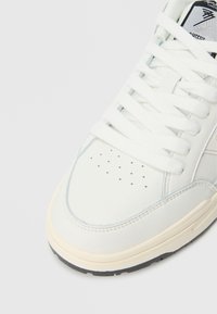 Λευκό δερμάτινο αθλητικό παπούτσι με επί�πεδα κορδόνια, διάτρητη μύτη και αντίθετη μπεζ σόλα. Διαθέτει υφασμένη πλευρική επιφάνεια και λογότυπο στη γλώσσα.