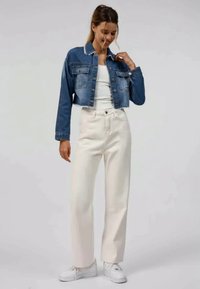 Jeansjakke med en kortet design, lys blå farge og hvite sømmer. Kombinert med høyt liv hvite bukser og hvite joggesko.