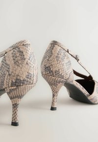 Klackar med ormskinnsmönster och spetsig tå, med justerbart rem och en smal stilettklack, med en texturerad yta i beige och grå nyanser.