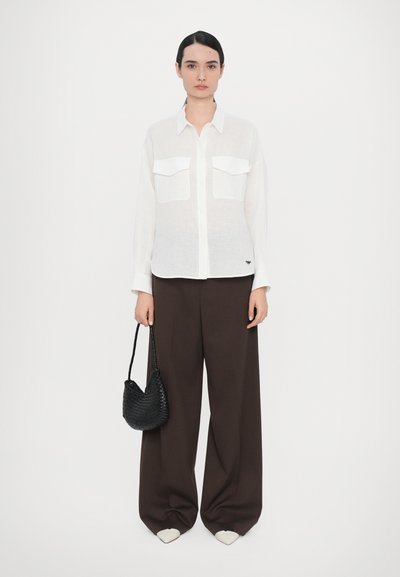 White, lightweight, long-sleeve shirt with two front pockets paired with dark brown wide-leg trousers and a small black woven handbag.