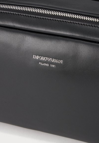 Μαύρη δερμάτινη τσάντα Emporio Armani με ασημένιο φερμουάρ και λογότυπο με κείμενο ""Emporio Armani Milano 1981"" στην εμπρόσθια επιφάνεια.