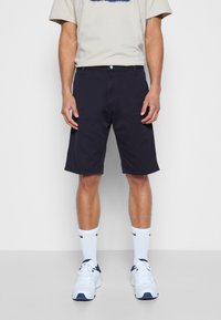 Calções de algodão azul marinho com um corte regular, reto e bolsos. Combinados com uma t-shirt de cor clara e ténis brancos.