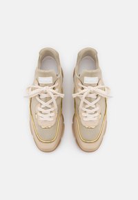 Beige sneakers med ett slätt, strukturerat canvas-överdel, snörning och gulddetaljer längs kanten på sulan. Transparent gummisula.