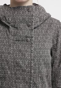 Gray patterned jacket with a hood, featuring geometric designs, metal snap buttons, and two front pockets. Textured fabric with visible stitching.