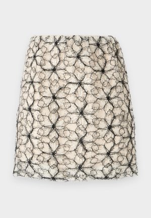 Fustă mini bej cu un strat superior de dantelă neagră asemănătoare unei pânze, cu modele neregulate hexagonale și stelate și fire texturate, pufoase.