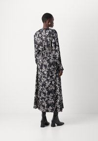 Crna haljina s dugim rukavima i cvjetnim uzorkom u bijeloj boji, strukirana, od lepršavog materijala i midi dužine. Uparena s crnim čizmama na petu.