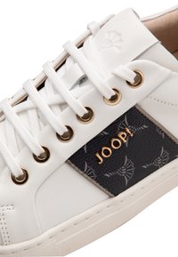 Sneaker in pelle bianca con un pannello laterale a motivo nero, occhielli dorati e lacci bianchi piatti con branding in rilievo sulla parte superiore.