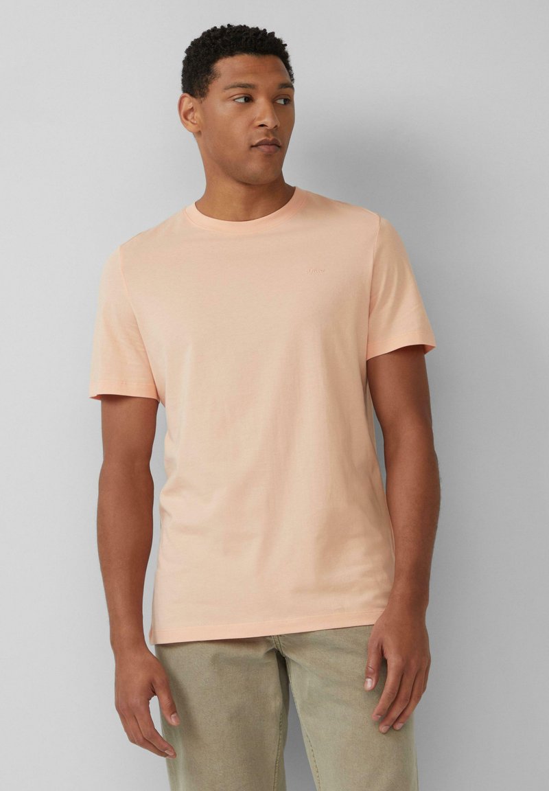 Korte mouwen, ronde hals t-shirt van zacht perzikkleurig materiaal. Heeft een subtiele logo op de borst en een standaard pasvorm. Licht textuur, casual ontwerp.