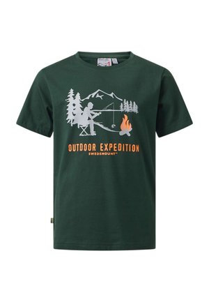 Garçon portant un t-shirt vert foncé « Outdoor Expedition », un pantalon cargo foncé, des bottes noires, tenant une veste noire, debout devant un fond blanc.