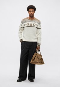 Άσπρο πουλόβερ με σχέδια και καφέ λεπτομέρειες, με σχέδια ταράνδων, συνδυασμένο με μαύρο παντελόνι και καφέ τσάντα σακίδιο.