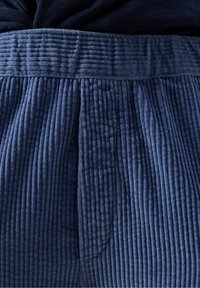 Modrá manžestrová tkanina s vertikálnymi ryhami, zložená a nariasená v strede, zobrazujúca textúru a detaily šitia.