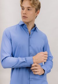 Lyseblå langermet skjorte med knappet krage, glatt tekstur og blå knapper, med en tettsittende design og justerbare mansjetter.