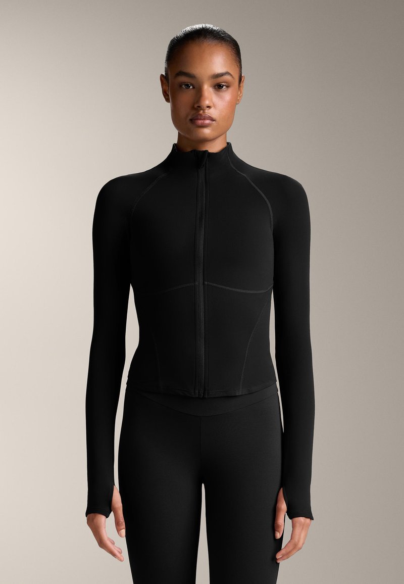 Schwarze, langärmlige Zip-Jacke mit hohem Kragen, die eine taillierte Passform und Flachnähte aufweist. Glatte Textur, minimalistischer Stil.