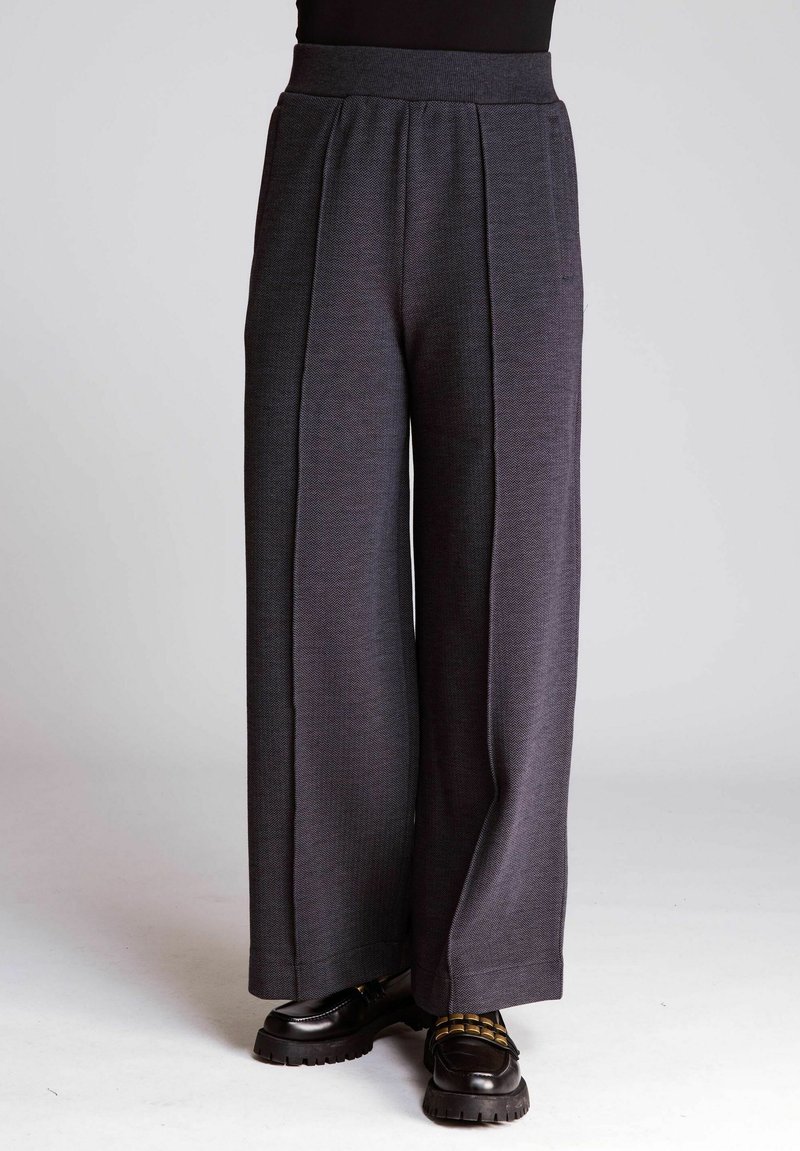 Wide-leg trousers in dark gray textured fabric, featuring a high waistband and front pleats, paired with black chunky-soled shoes.