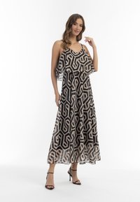 Maxi mekko mustalla, beigen ja kullan värisillä geometrisillä kuvioilla, kerroksellisella valuvalla suunnittelulla, säädettävillä olkaimilla ja yhdistettynä mustiin remmisandaaleihin.