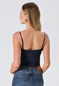 Camisola blu navy con spalline sottili regolabili, design aderente e consistenza liscia. Abbinata a jeans in denim a vita alta con tasche applicate.